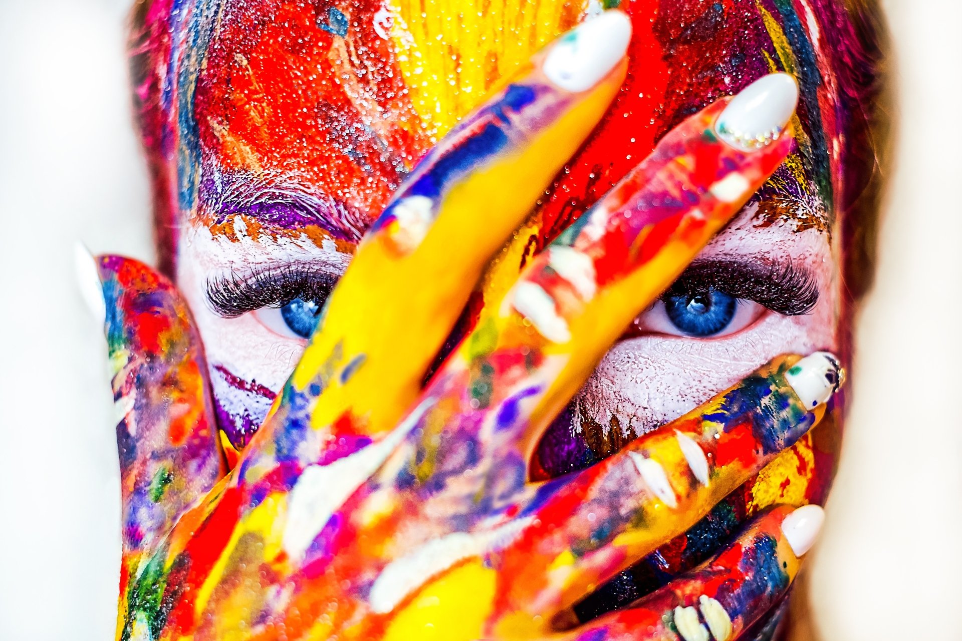 Close-up 4K Ultra HD PC desktop wallpaper of a woman's painted face and hand in vivid colors, fingers partially covering one eye to reveal bright blue eyes.