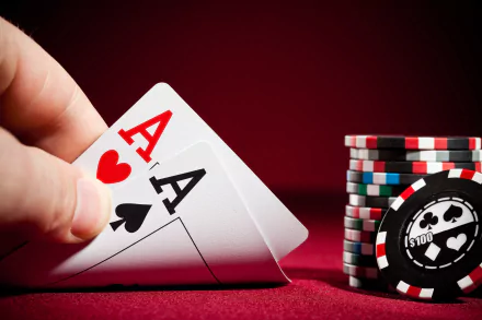 HD desktop wallpaper showing a man-made poker scene with a hand holding two aces and a stack of colorful poker chips on a red surface.