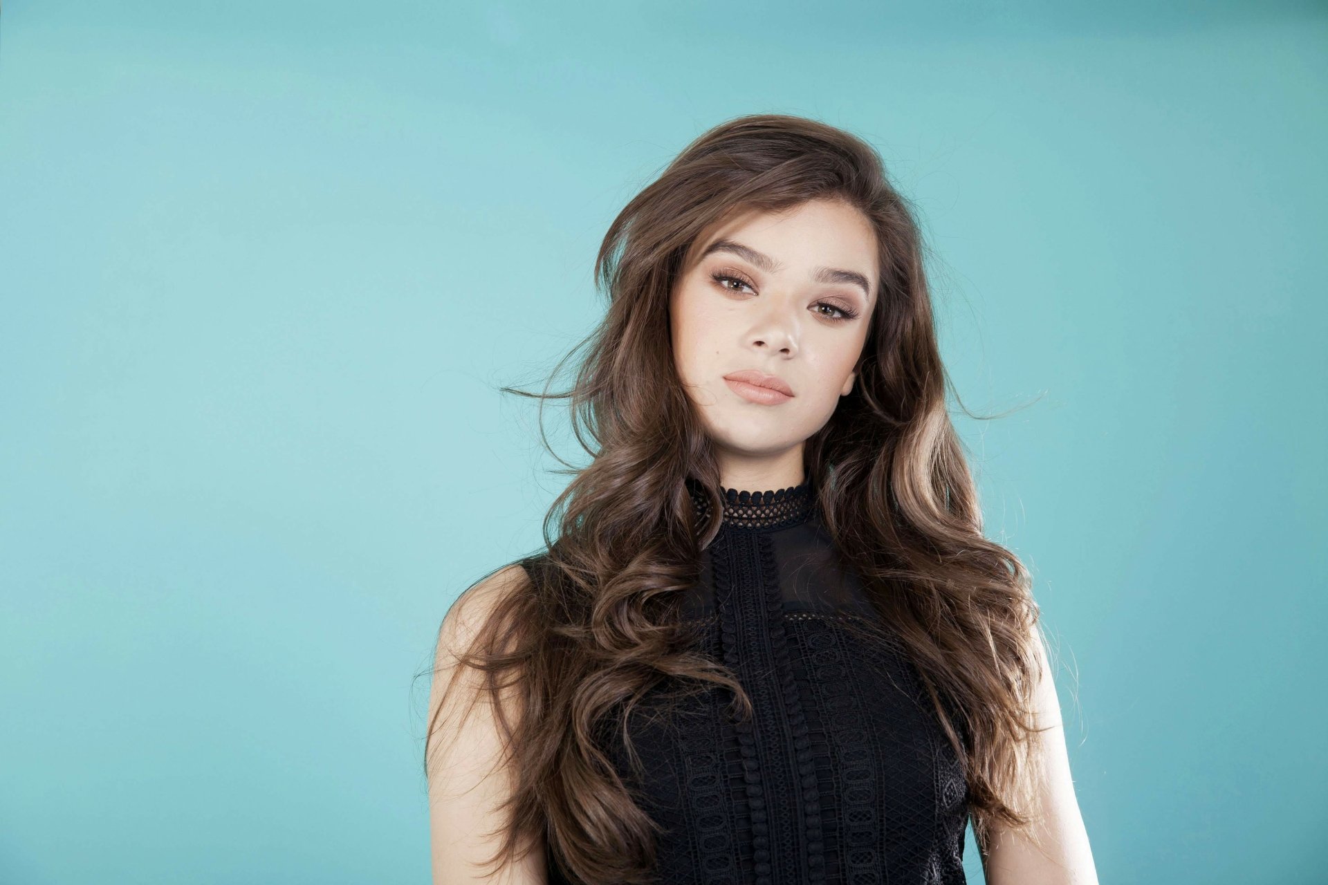 Portrait of American actress Hailee Steinfeld with long brunette hair against a soft blue background in 4K Ultra HD resolution.